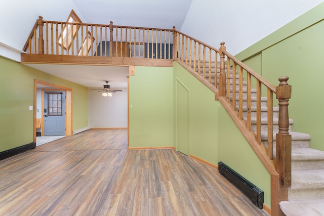 staircase with hardwood / wood-style floors, high vaulted ceiling, baseboard heating, and ceiling fan