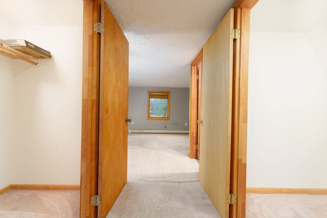 corridor with light colored carpet, a textured ceiling, and a baseboard heating unit