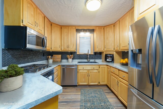 kitchen featuring decorative backsplash, appliances with stainless steel finishes, light brown cabinetry, sink, and light hardwood / wood-style floors