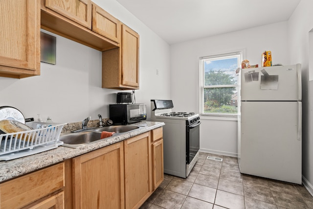 kitchen with sink, gas range oven, white fridge, light brown cabinetry, and light tile patterned flooring