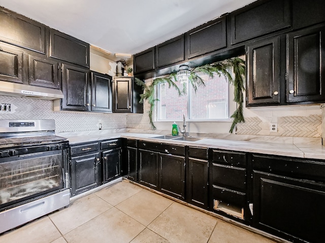 kitchen with backsplash, sink, stainless steel stove, and light tile patterned flooring