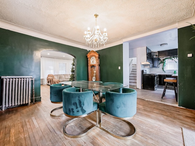 dining space featuring radiator heating unit, light wood-type flooring, a textured ceiling, and an inviting chandelier