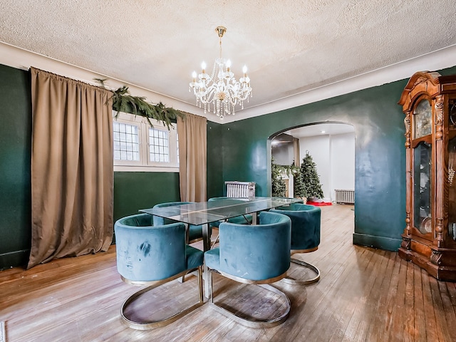 dining area with hardwood / wood-style floors, a textured ceiling, radiator, and a chandelier