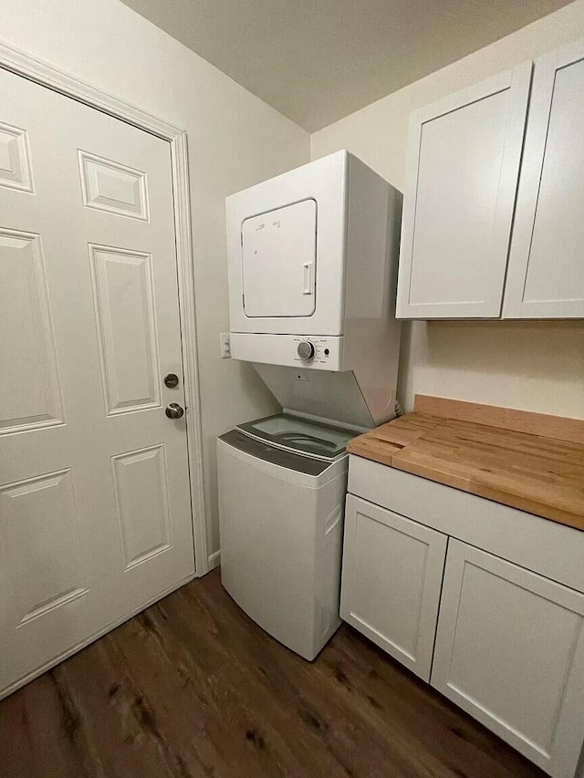 laundry room featuring stacked washer / dryer, cabinets, and dark hardwood / wood-style floors