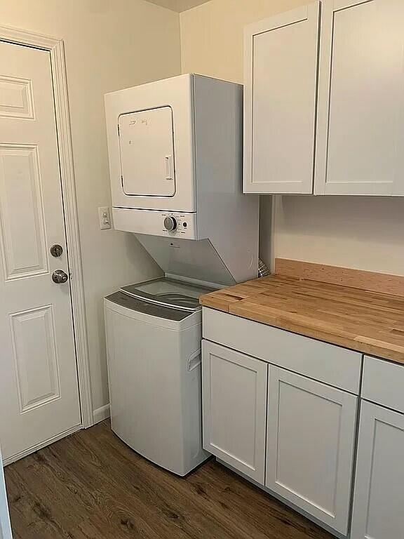 laundry room featuring cabinets, dark wood-type flooring, and stacked washer and clothes dryer