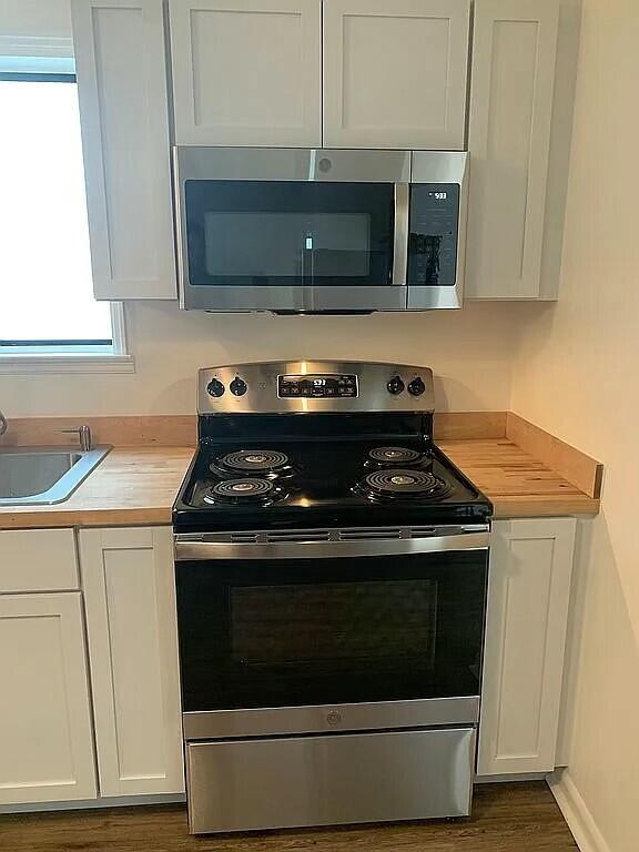 kitchen featuring butcher block counters, dark wood-type flooring, sink, appliances with stainless steel finishes, and white cabinetry