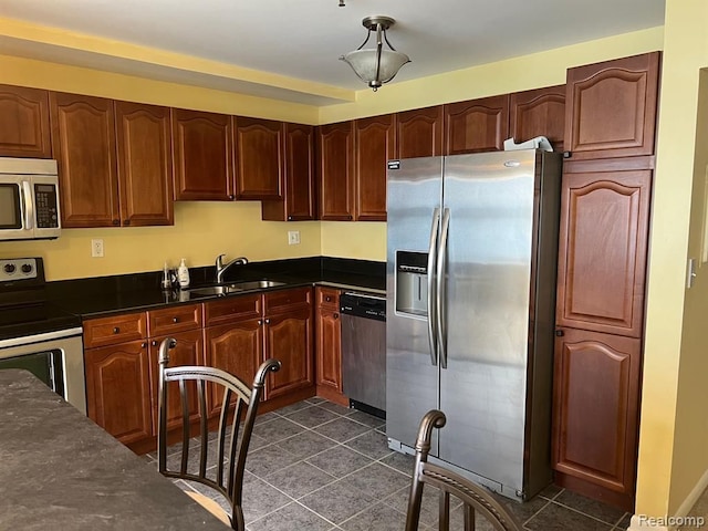 kitchen featuring stainless steel appliances, dark countertops, a sink, and dark tile patterned floors