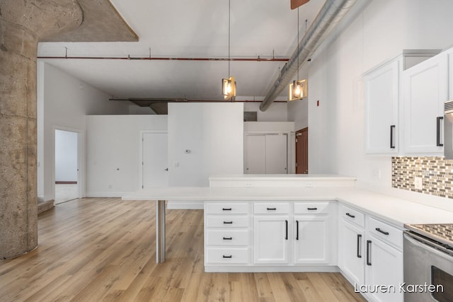 kitchen featuring a towering ceiling, light wood-type flooring, white cabinetry, and hanging light fixtures