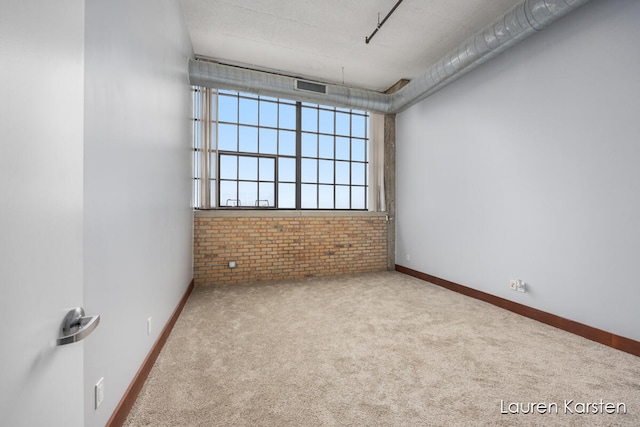 empty room featuring light carpet, a textured ceiling, and brick wall