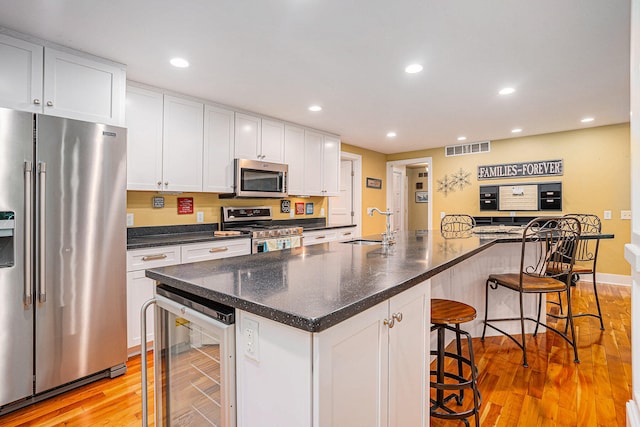 kitchen featuring stainless steel appliances, beverage cooler, a breakfast bar area, and a kitchen island with sink