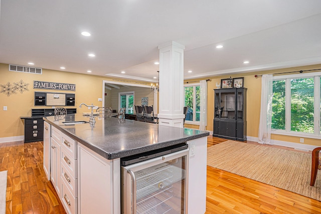 kitchen featuring decorative columns, wine cooler, light hardwood / wood-style flooring, and white cabinets