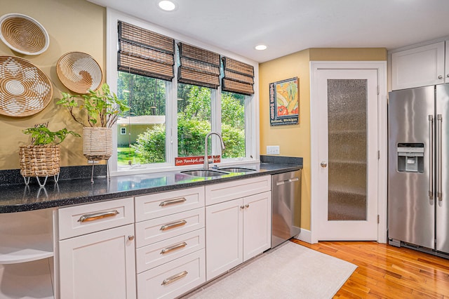 kitchen with white cabinetry, sink, dark stone countertops, appliances with stainless steel finishes, and light wood-type flooring