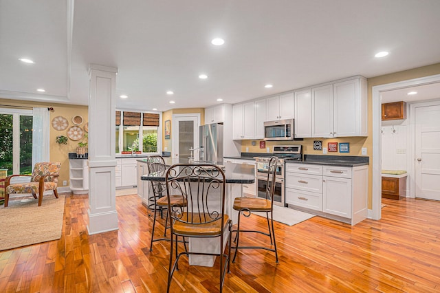 kitchen featuring appliances with stainless steel finishes, light hardwood / wood-style flooring, ornate columns, and a wealth of natural light