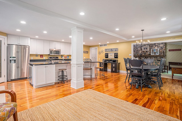 dining space featuring decorative columns, a chandelier, light hardwood / wood-style floors, and ornamental molding