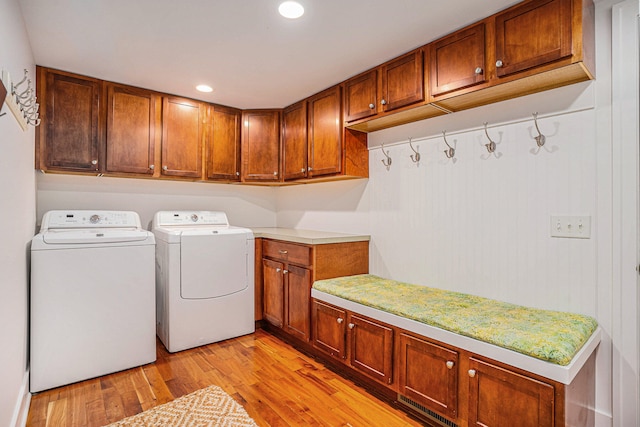 clothes washing area with separate washer and dryer, light hardwood / wood-style flooring, and cabinets