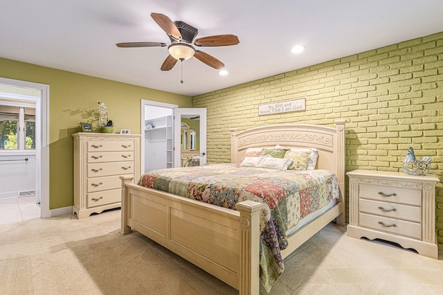 carpeted bedroom with a walk in closet, a closet, ceiling fan, and brick wall