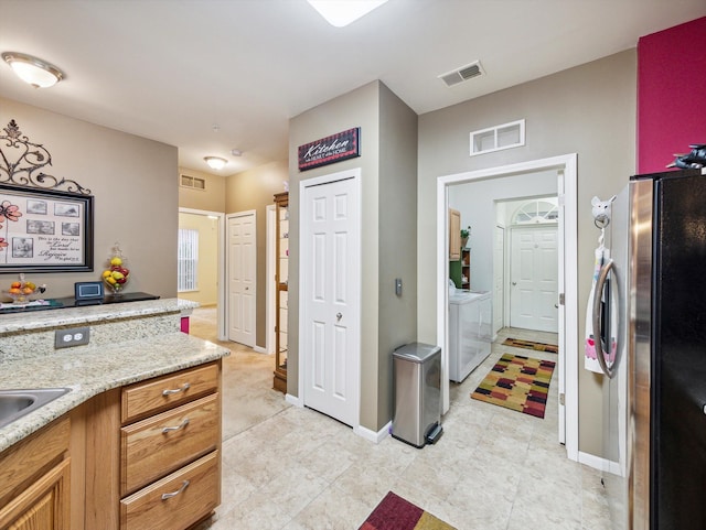 kitchen with stainless steel fridge, light stone countertops, and independent washer and dryer