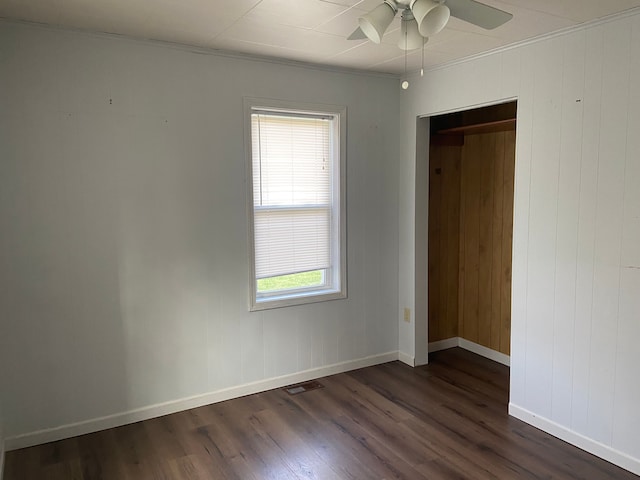 empty room featuring wooden walls, dark hardwood / wood-style flooring, ceiling fan, and ornamental molding