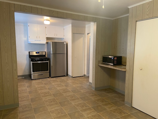 kitchen with white cabinetry, crown molding, wood walls, and appliances with stainless steel finishes