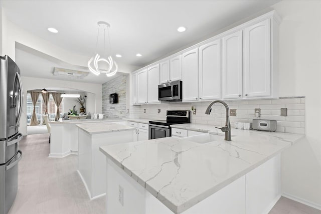 kitchen with kitchen peninsula, pendant lighting, stainless steel appliances, and light stone countertops