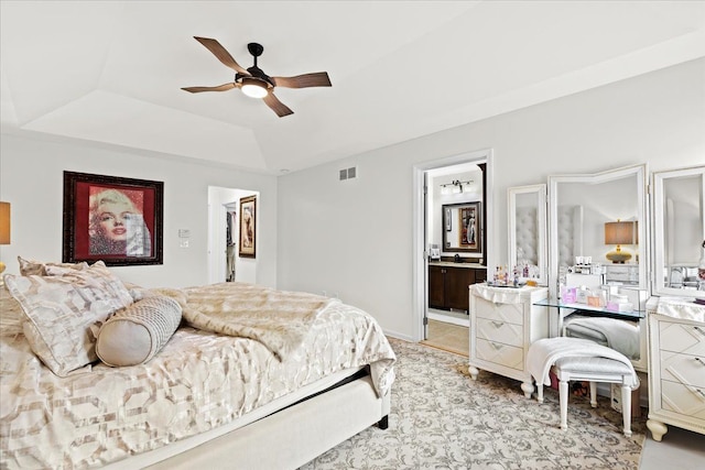 bedroom featuring a tray ceiling, ensuite bathroom, ceiling fan, and light carpet