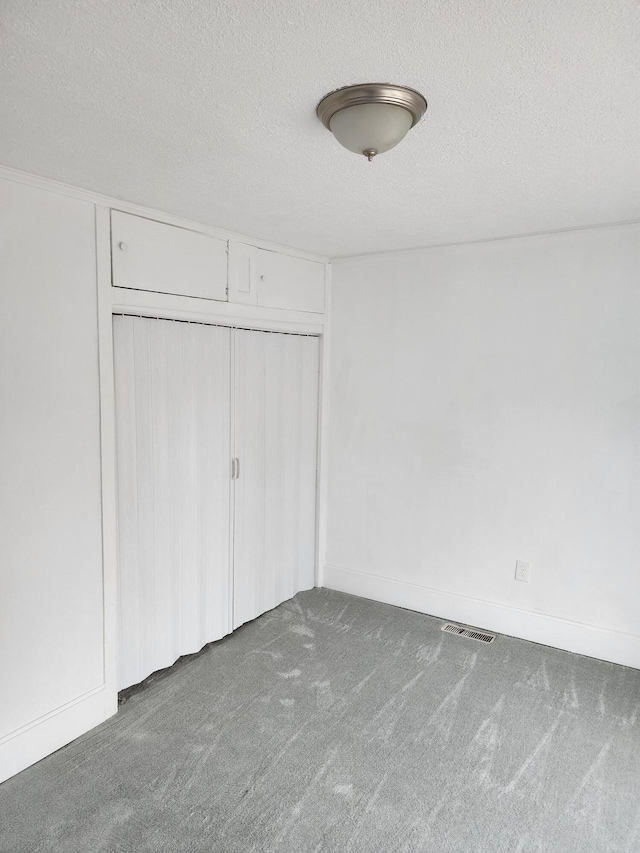 interior space featuring a textured ceiling, dark carpet, and a closet