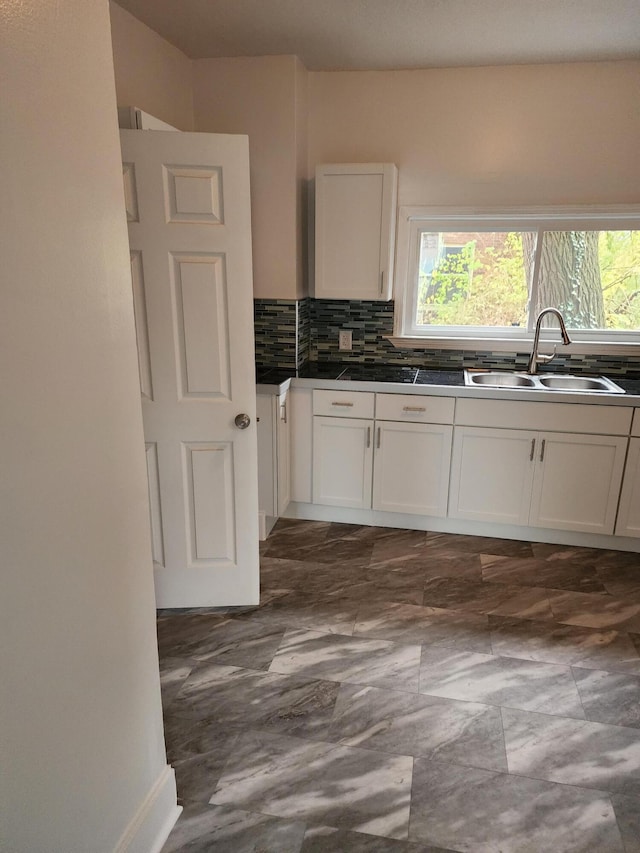 kitchen featuring decorative backsplash, white cabinetry, and sink