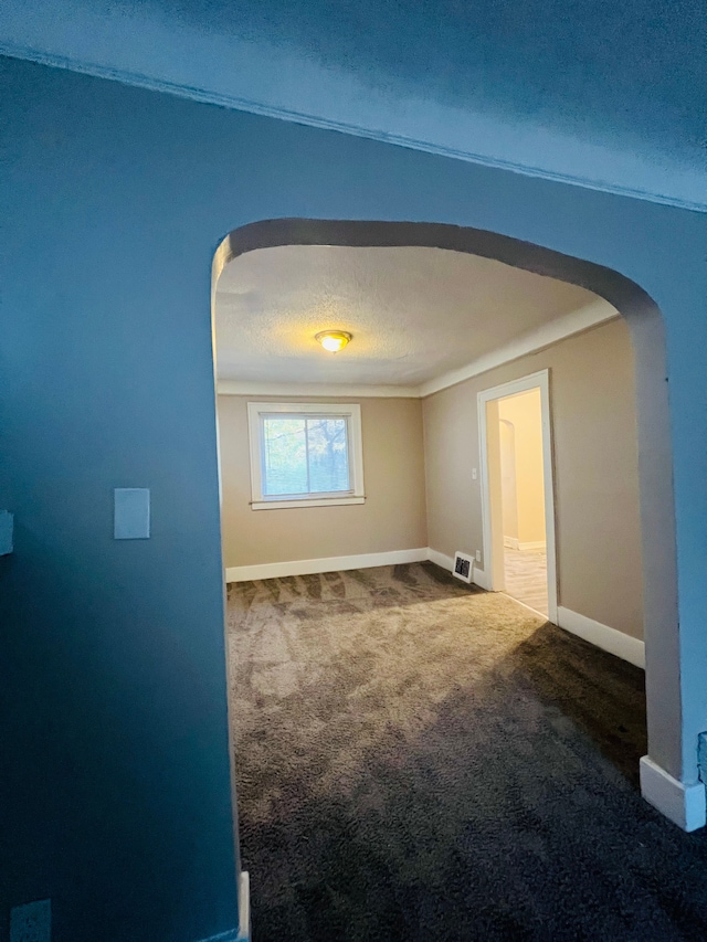 empty room featuring dark carpet, a textured ceiling, and ornamental molding