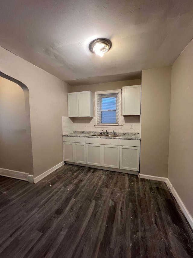 kitchen with white cabinetry, sink, dark wood-type flooring, light stone counters, and backsplash