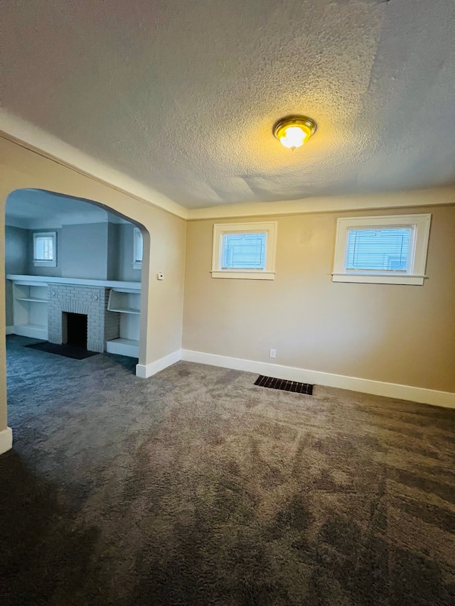 carpeted spare room with a textured ceiling and a brick fireplace