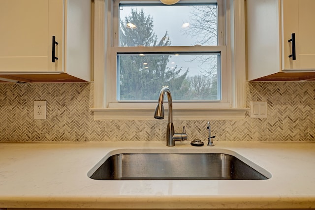 interior details featuring decorative backsplash, white cabinetry, light stone countertops, and sink