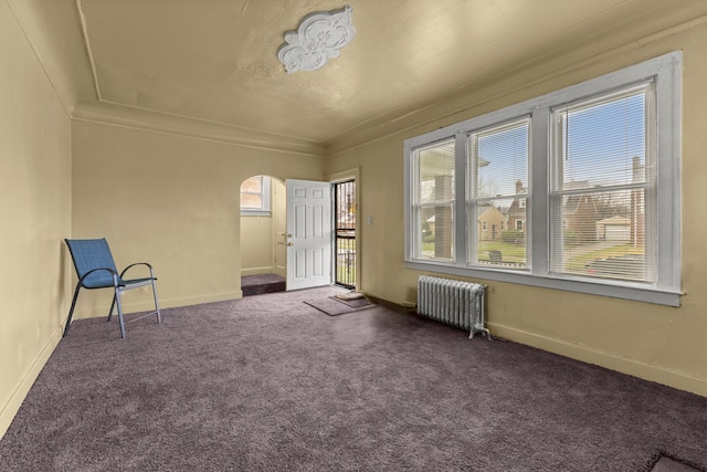 interior space featuring dark colored carpet, radiator heating unit, crown molding, and a healthy amount of sunlight