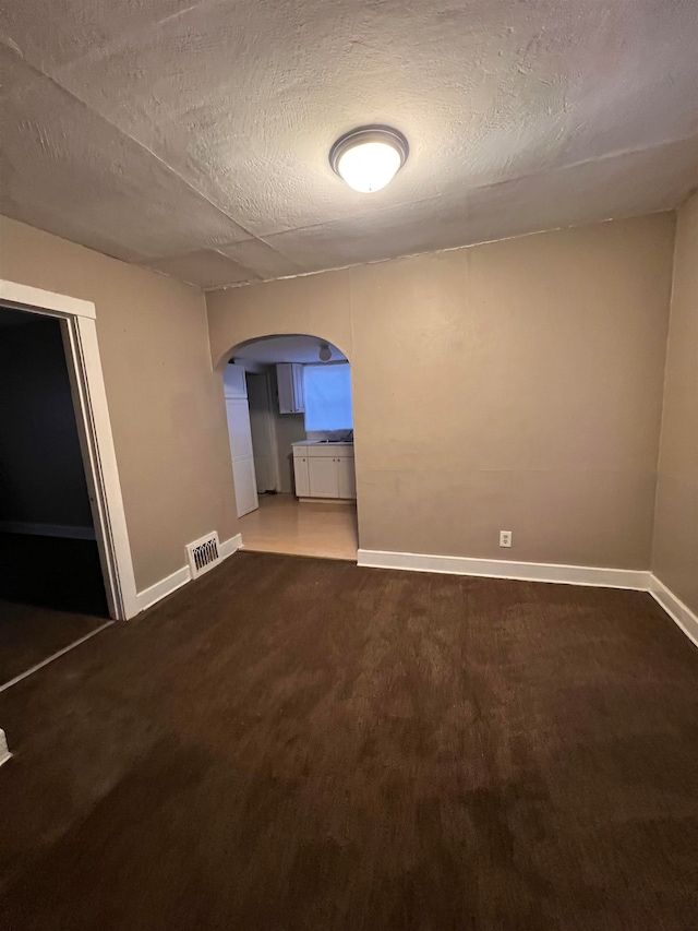 unfurnished room with a textured ceiling and dark carpet