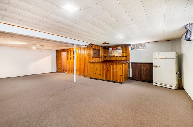 finished below grade area featuring wooden walls, freestanding refrigerator, and light colored carpet