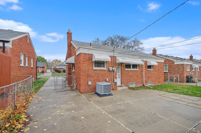 rear view of property with brick siding, a chimney, a gate, central AC, and fence