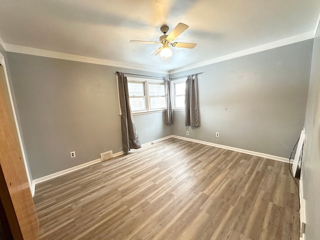 empty room featuring wood finished floors, a ceiling fan, baseboards, visible vents, and crown molding