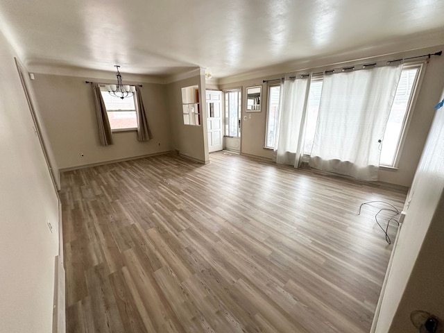 unfurnished living room with baseboards, light wood-type flooring, and a notable chandelier