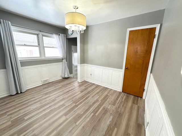 unfurnished dining area featuring a chandelier, a wainscoted wall, visible vents, and light wood finished floors