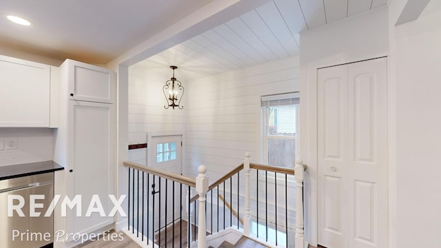 stairway featuring wood walls, wood-type flooring, and an inviting chandelier