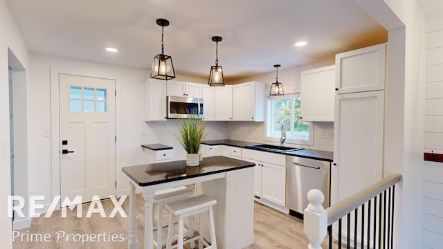 kitchen featuring white cabinetry, sink, hanging light fixtures, light hardwood / wood-style floors, and appliances with stainless steel finishes