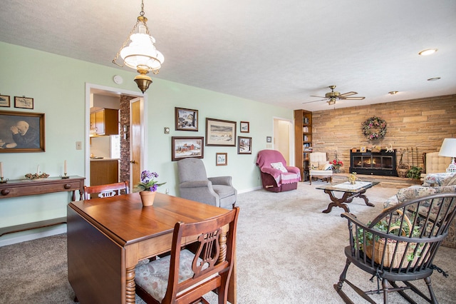 dining space with a textured ceiling, carpet floors, a stone fireplace, and ceiling fan