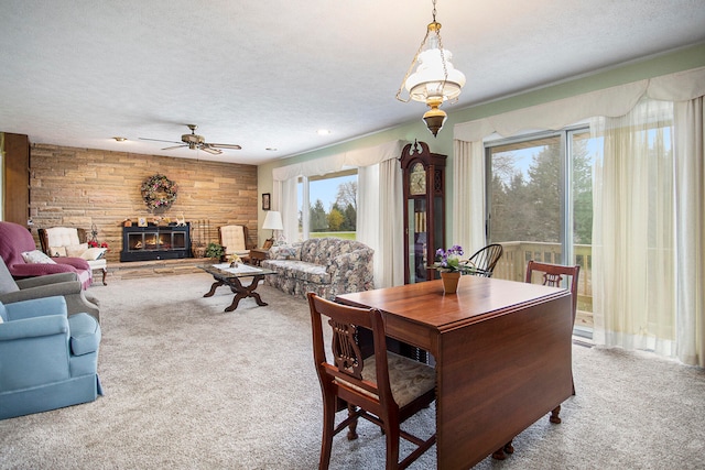 carpeted dining space with a textured ceiling, ceiling fan, a fireplace, and wooden walls