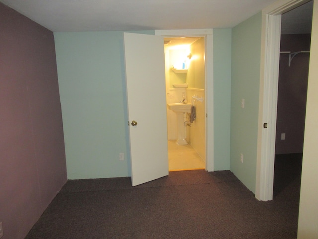 unfurnished bedroom with dark colored carpet, a walk in closet, ensuite bath, and a closet