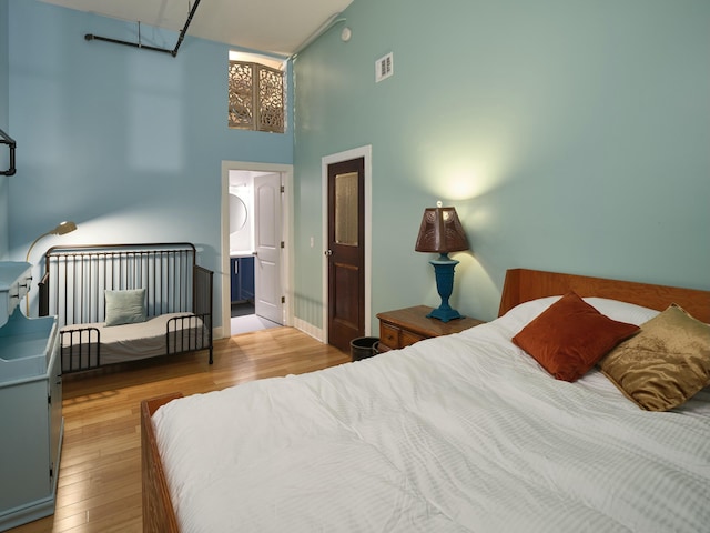 bedroom with connected bathroom, a high ceiling, and light hardwood / wood-style flooring