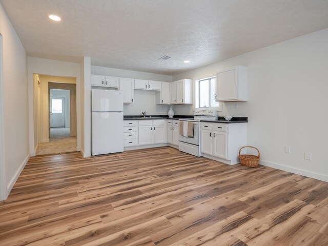 kitchen with a textured ceiling, white appliances, white cabinetry, and light hardwood / wood-style floors