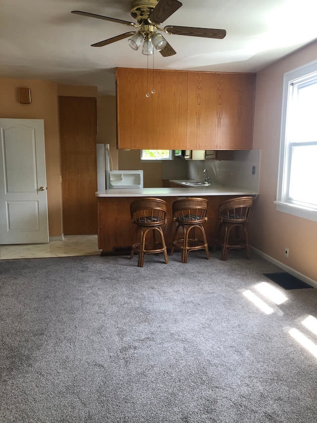 kitchen featuring a kitchen breakfast bar, refrigerator, carpet flooring, ceiling fan, and kitchen peninsula