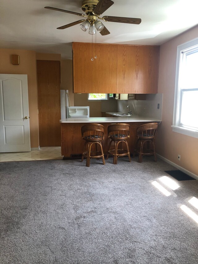 212 15th St, Port Huron, MI 48060 - kitchen featuring brown cabinetry, a ceiling fan, a kitchen breakfast bar, light countertops, and carpet floors