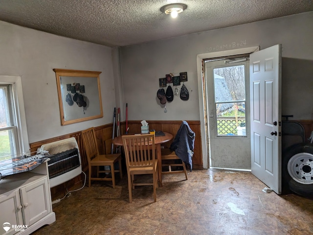 dining room featuring heating unit, wood walls, plenty of natural light, and a textured ceiling