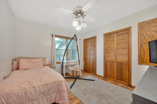 bedroom with ceiling fan, two closets, and light hardwood / wood-style flooring