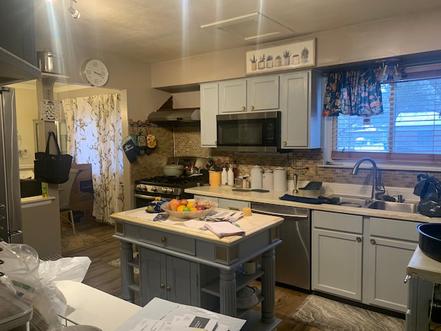 kitchen with appliances with stainless steel finishes, gray cabinetry, dark wood-type flooring, sink, and wall chimney range hood